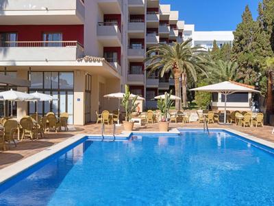 Blauer Swimmingpool vor einem mehrstöckigen Hotel mit Sonnenschirmen und Palmen.