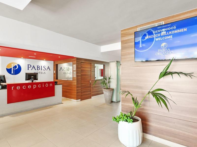 Moderní hotelová lobby s červenou recepcí a digitálním displejem na stěně.