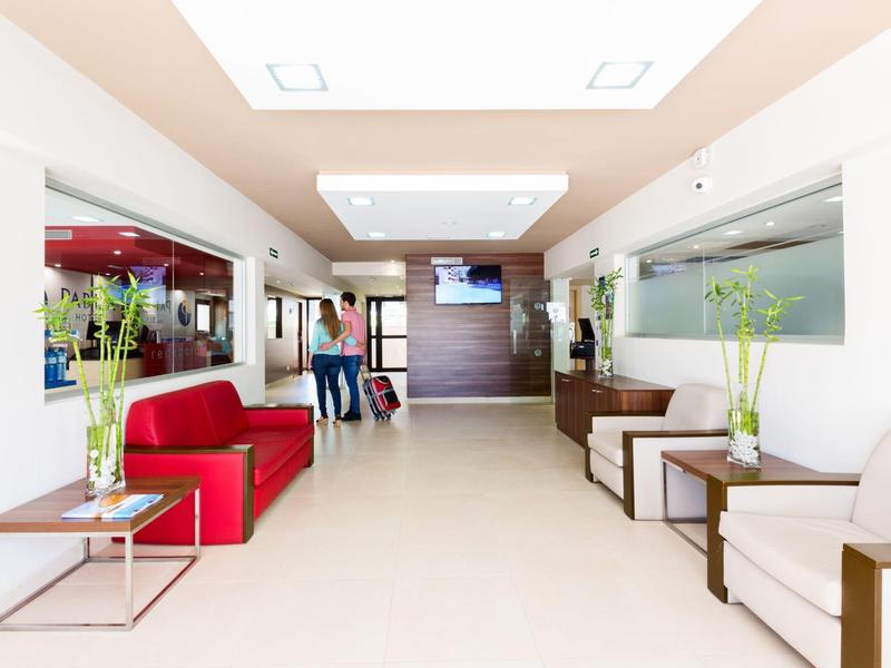 Světlá hotelová hala s bílými stěnami, červenou pohovkou a moderním osvětlením.