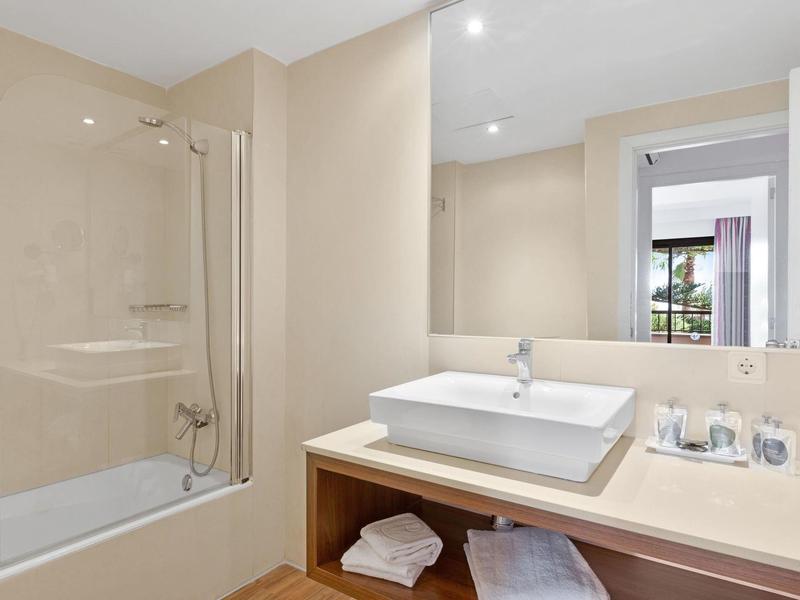 Moderní koupelna s vanou, umyvadlem a velkým zrcadlem v světlých barvách.