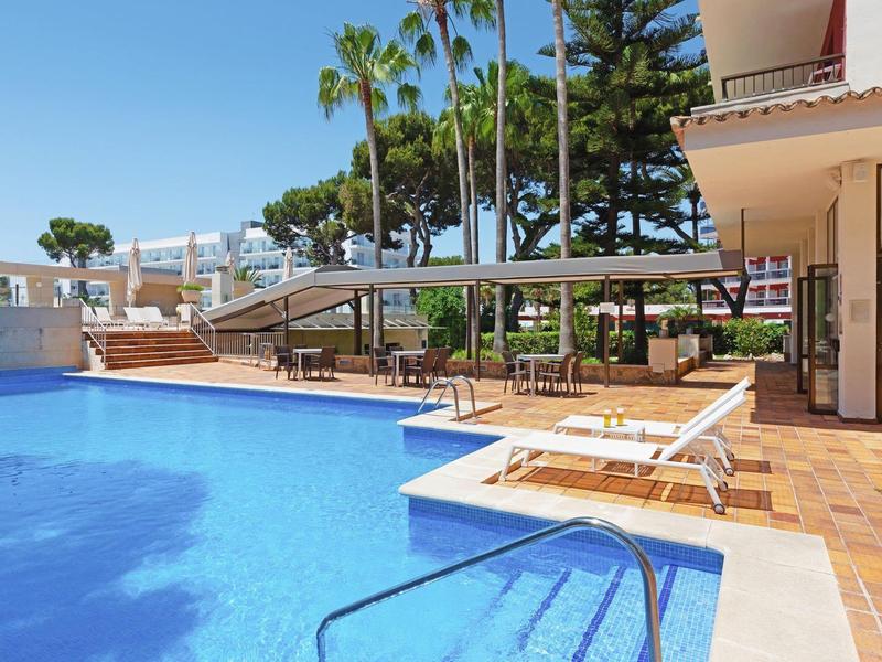 Moderní venkovní bazén s lehátky a palmami v slunném hotelovém prostředí.