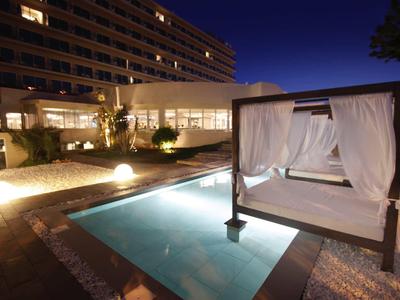 Piscina dell'hotel illuminata con lettino e tende al crepuscolo.
