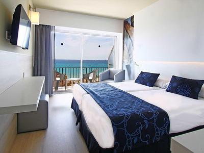 Camera d'hotel luminosa con letto grande e vista mare tramite porta scorrevole.