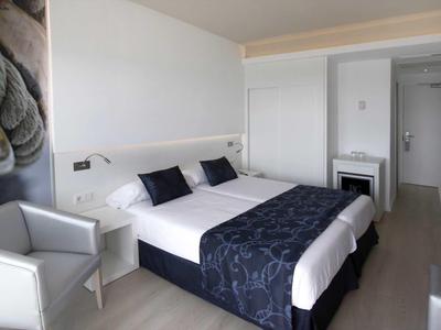 Camera d'hotel moderna con letto matrimoniale, area salotto e colori neutri.