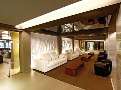 Hall di un hotel moderno con divani bianchi, tavoli in legno e illuminazione soffusa.