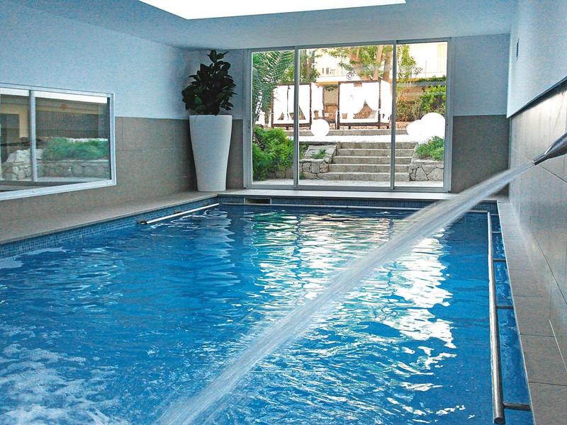 Una piscina coperta luminosa con un getto d'acqua e vista su un'area esterna.