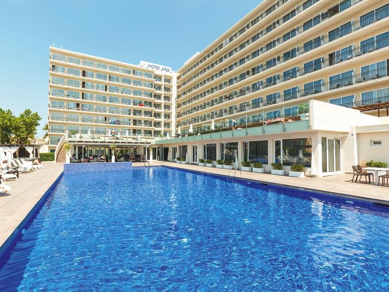 Grande piscina blu davanti a un hotel moderno su più piani con lettini prendisole.