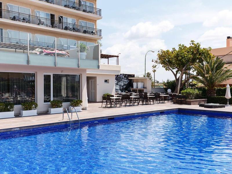 Piscina moderna dell'hotel con lettini e piante sotto un cielo azzurro