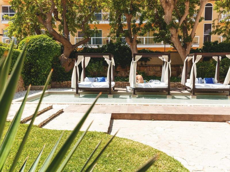 Quattro lettini bianchi con cuscini blu accanto a una piscina in un giardino dell'hotel.