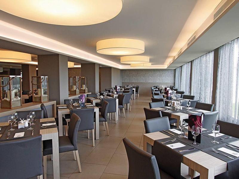 Sala da pranzo moderna dell'hotel con sedie grigie e luce naturale da grandi finestre.