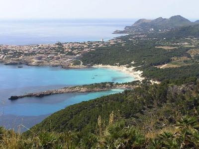 Küstenlandschaft mit türkisblauem Meer, felsiger Landzunge und bewaldeten Hügeln im Vordergrund.
