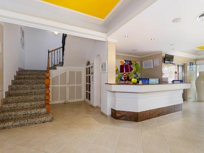 Lichte hotellobby met receptiebalie, grote vazen en een trap met tapijt.