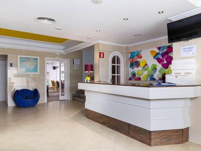 Modern hotel lobby with white reception desk, colorful wall art, and blue armchair.