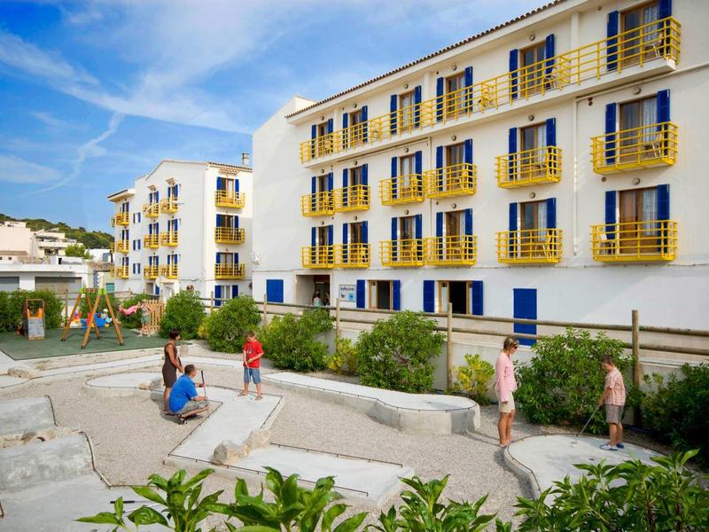 Modern hotelgebouw met balkons naast een kleine speeltuin en zithoek