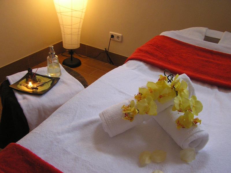 Een spabehandelingsruimte met een wit bed, rode accenten en decoratieve orchideeënblaadjes.