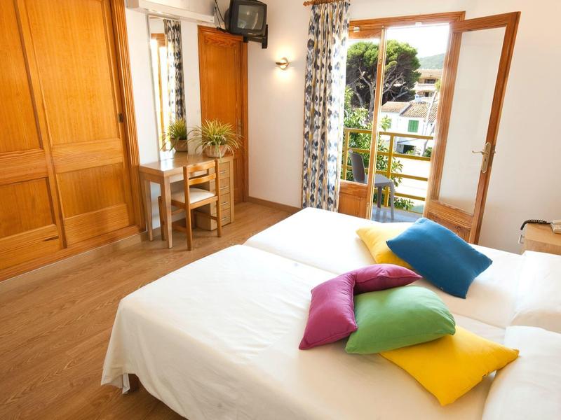 Lichte hotelkamer met tweepersoonsbed, kleurrijke kussens en open balkon met uitzicht op tuin.