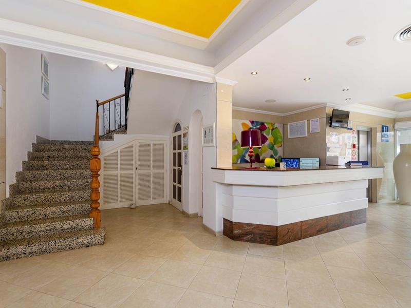 Lichte hotellobby met receptiebalie, grote vazen en een trap met tapijt.