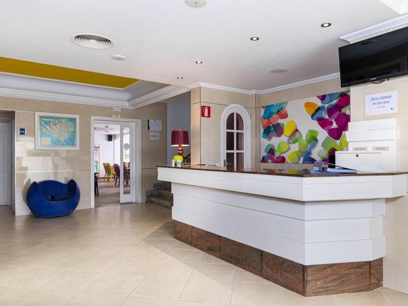 Lichte hotelreceptie met modern bureau en kleurrijke wanddecoratie.