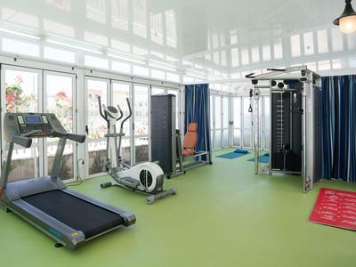Moderner Fitnessraum mit Laufband, Crosstrainer und Kraftstation vor großen Fenstern.