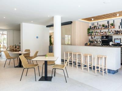 Nowoczesny bar i jadalnia z jasnymi drewnianymi krzesłami i jasnym oświetleniem.