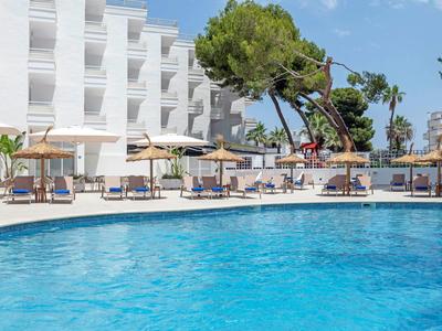 Jasnoniebieski basen przed nowoczesnym białym hotelem pod niebieskim niebem.