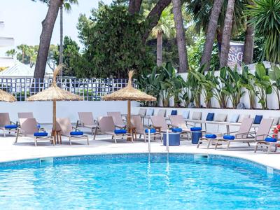 Niebieski basen otoczony leżakami i parasolami z trzciny pod palmami.