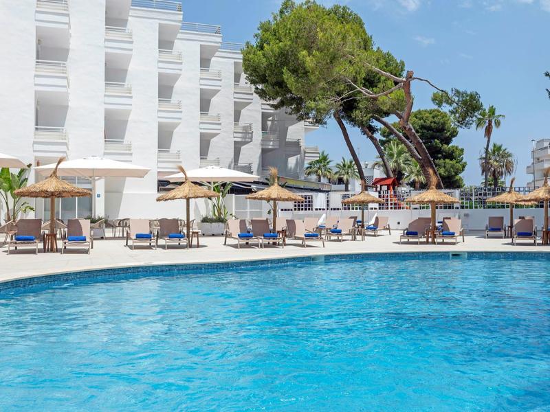 Jasnoniebieski basen przed nowoczesnym białym hotelem pod niebieskim niebem.