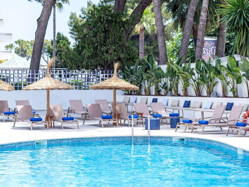 Niebieski basen otoczony leżakami i parasolami z trzciny pod palmami.