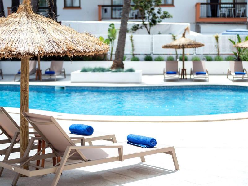 Basen hotelowy z leżakami i niebieskimi ręcznikami pod słomianymi parasolami.