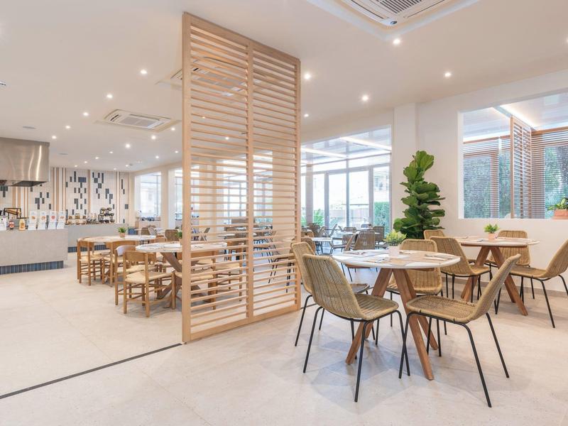 Nowoczesna jadalnia z drewnianymi stołami i krzesłami przy ażurowej ściance.