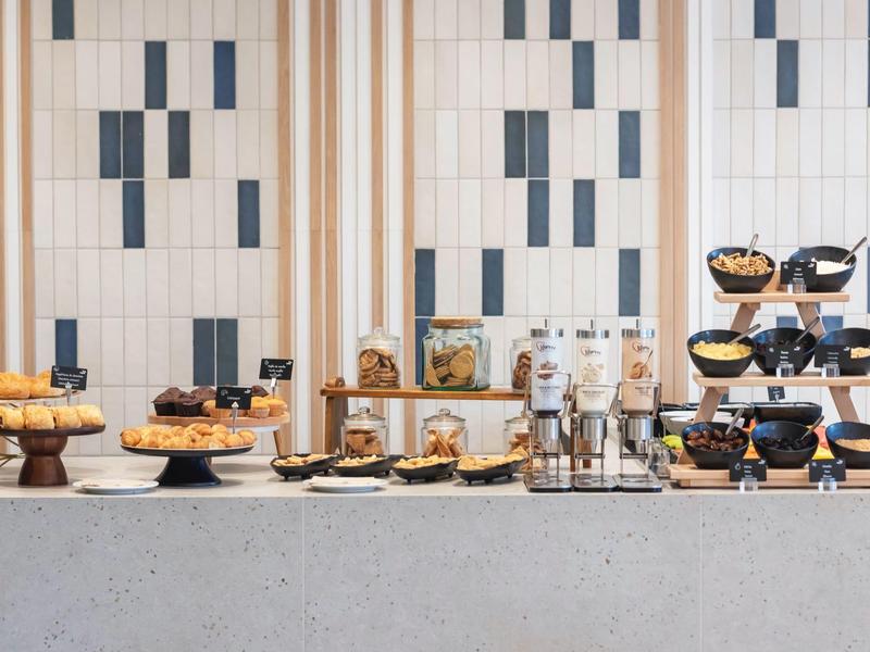 Bufet z ciastkami i płatkami śniadaniowymi w nowoczesnym wnętrzu z białymi i brązowymi kafelkami.