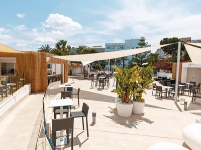 Open rooftop terrace with seating, sun sails, and plants under clear sky.