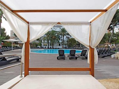 View from a covered pool lounger overlooking a pool area with sunbeds and palm trees.