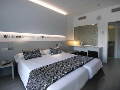 Modern hotel room with double bed, gray carpet, nightstands, and indirect lighting.