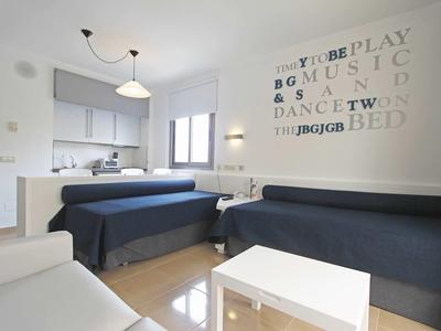 Modern hotel room with two single beds, sofa, and kitchenette.