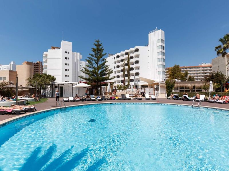 Large round pool in front of a white hotel building under a sunny sky.