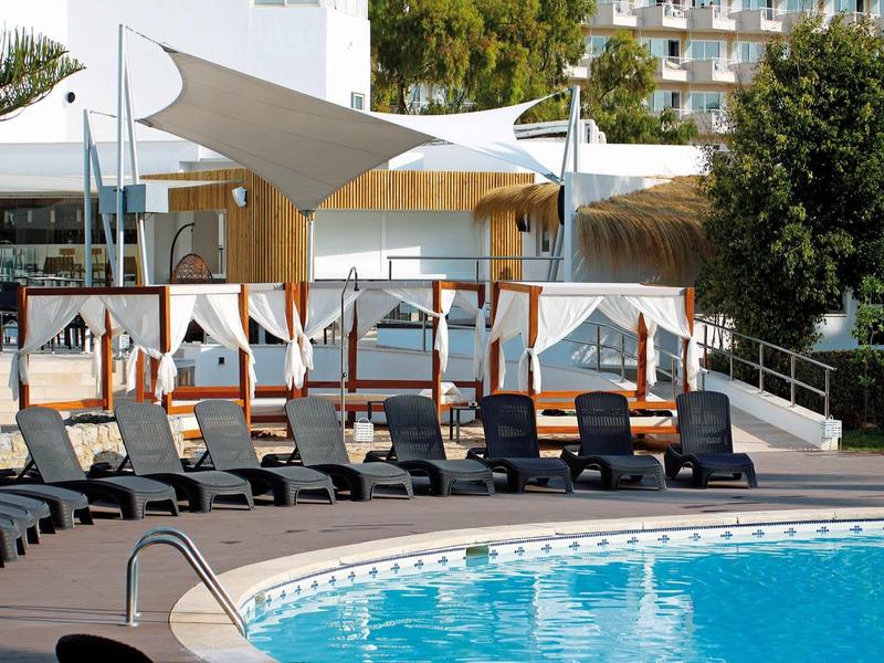 Several sun loungers next to a pool with sun shades at the hotel.
