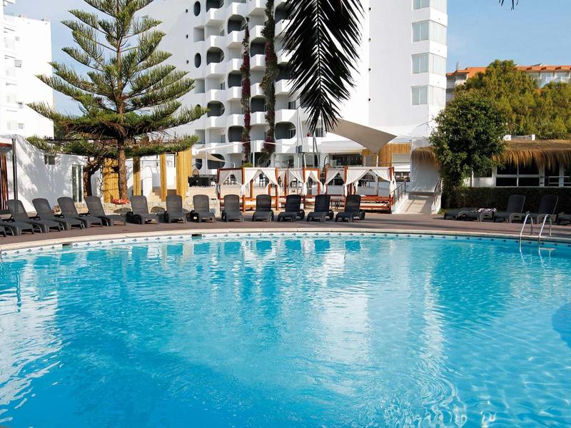 Large hotel pool with blue water surface and lounge chairs in the sunshine.