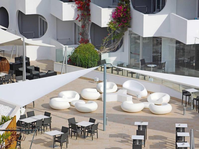 Modern outdoor area with white seats and black tables in front of a white hotel building.