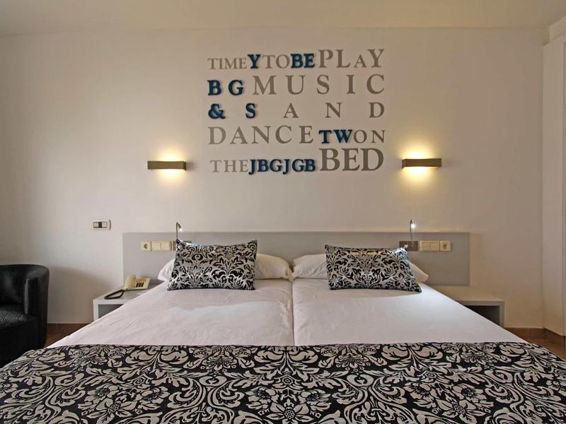 Modern bedroom with double bed, decorative pillows, and letter wall decoration.