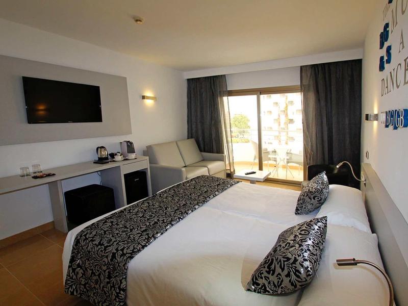 Modern hotel room with two beds, desk, television, and balcony with outdoor view.