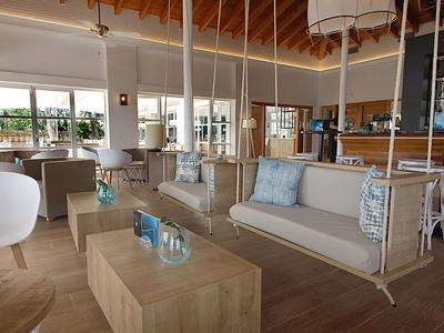 Nowoczesny hotelowy salon z wiszącymi sofami, drewnianymi stolikami i dużymi oknami z widokiem na morze.