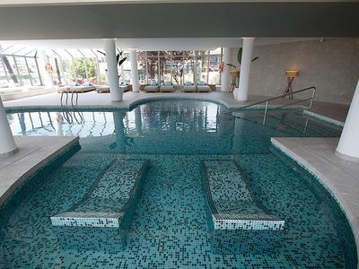 Innen gep?egtes Schwimmbad mit raumhohen Fenstern und Wassersitzbänken aus Mosaikfliesen.