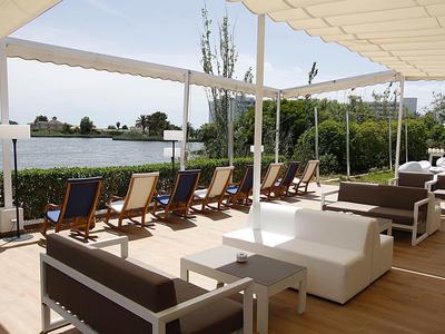 Modernes Outdoor-Lounge mit Sesseln und Liegestühlen am Wasser unter Sonnensegeln.