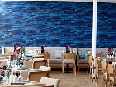 Modernes Restaurant mit Holztischen, beigen Stühlen und blauer Wand mit gemustertem Design.