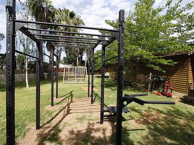 Zewnętrzny sprzęt fitness na zielonej trawie z palmami i budynkami w tle.