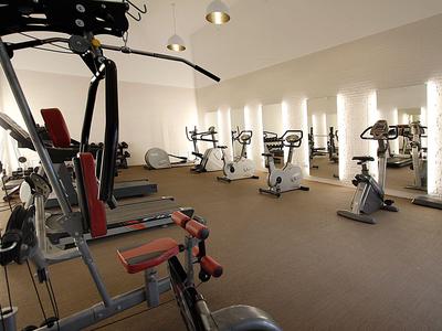 Siłownia z różnymi urządzeniami do ćwiczeń i rowerami stacjonarnymi przed oświetlonymi ścianami.