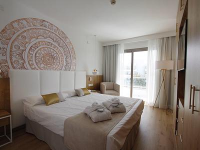 Helles Hotelzimmer mit Doppelbett, weißen Vorhängen und Balkonblick