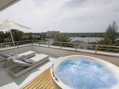 Moderne Terrasse mit Whirlpool, Liegen und Blick auf Wasser und Grünflächen