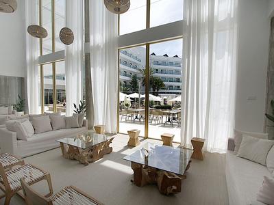 Jasna lobby hotelowa z wysokimi oknami, białymi zasłonami i nowoczesnymi drewnianymi meblami.